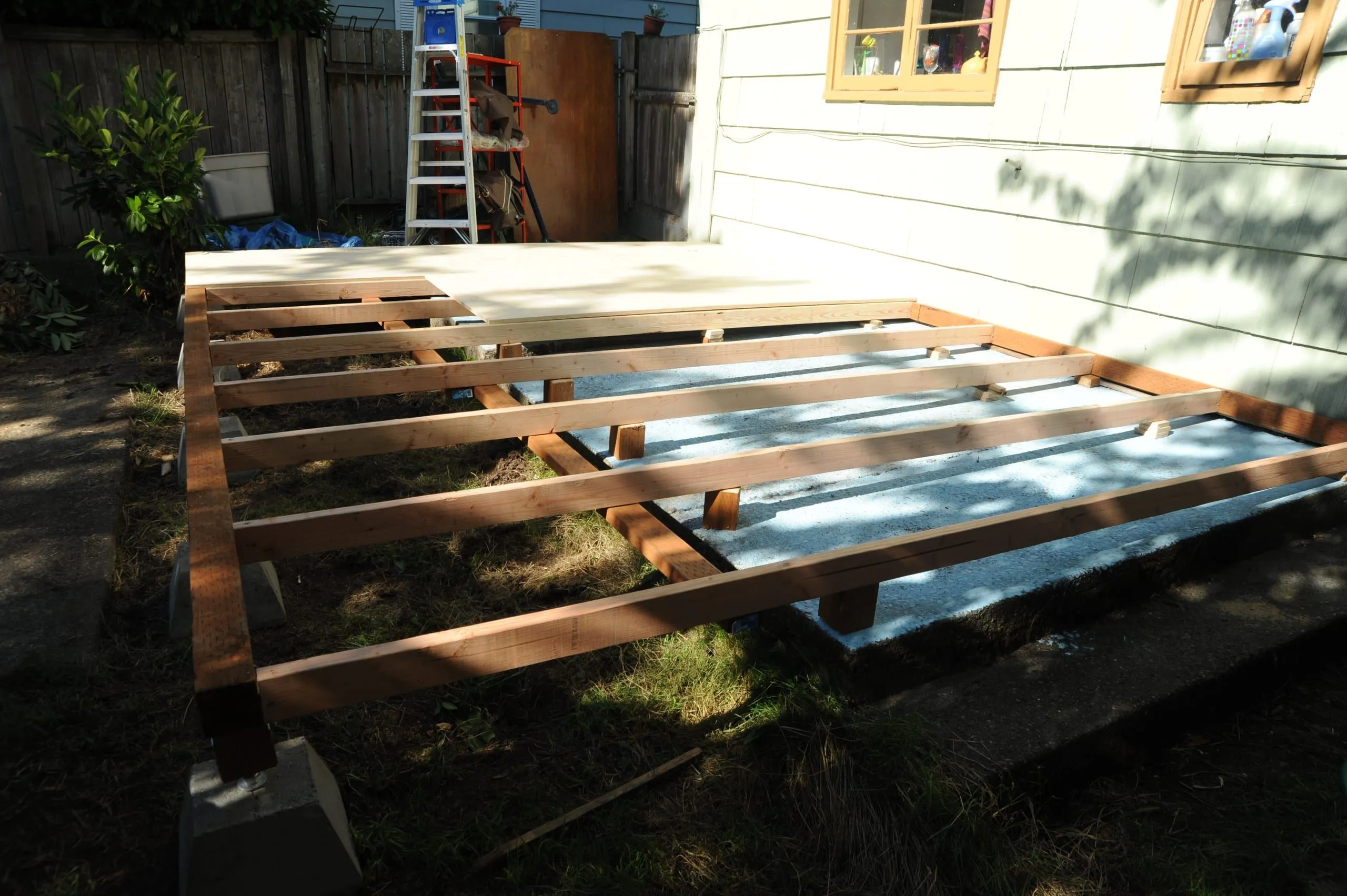 The timber frame of a deck, bearers and joists on concrete piers, being built beside a house