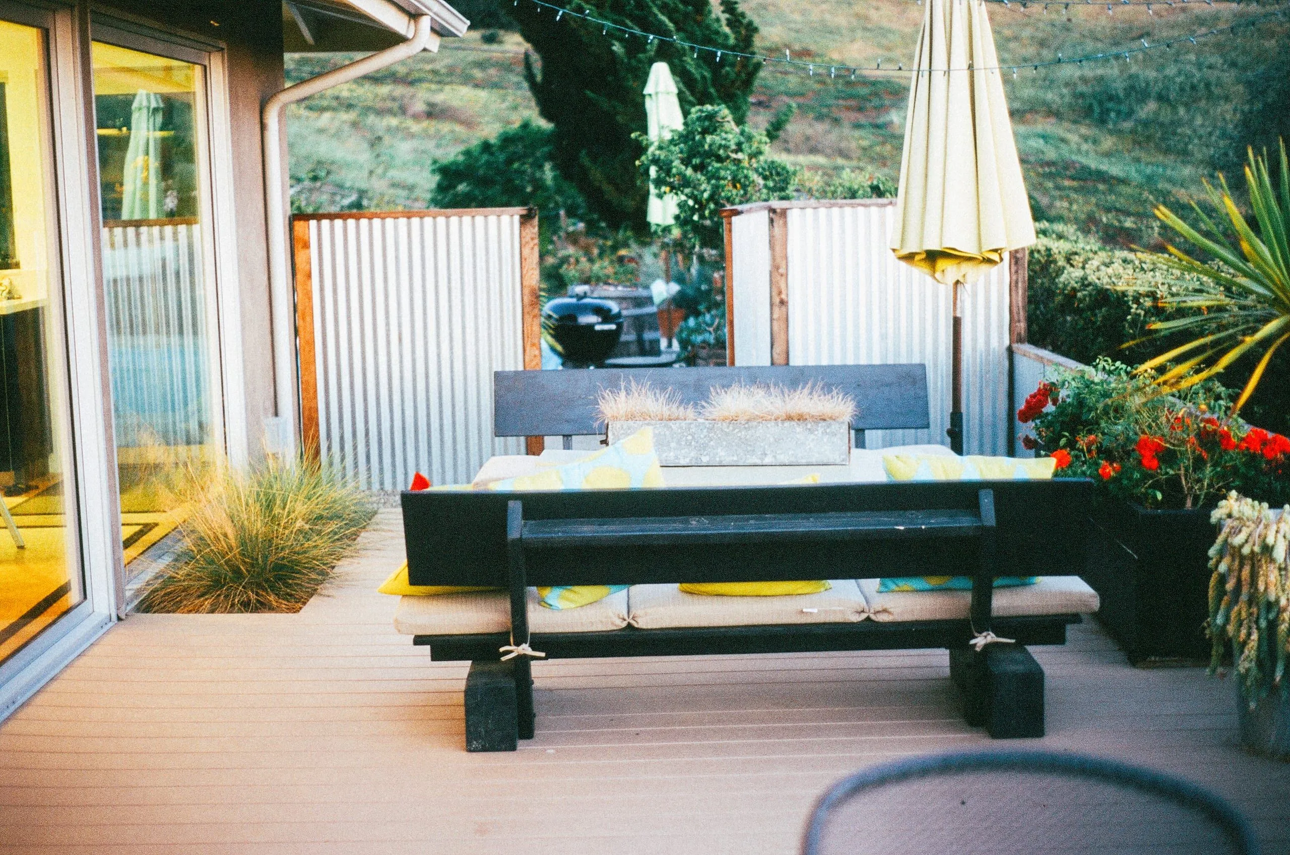 A composite deck with a black bench and table, a cream umbrella and corrugated iron privacy screens