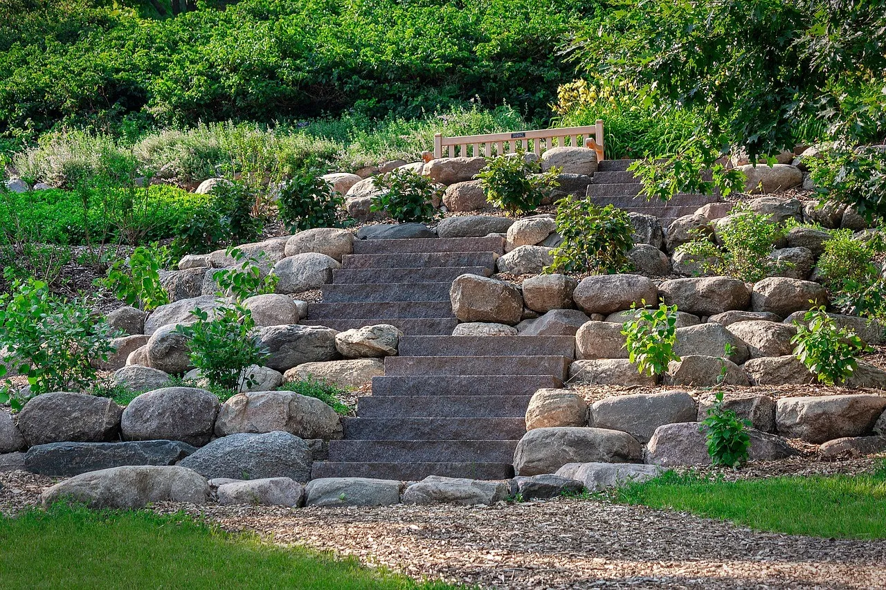 Wide granite steps rising between retaining walls of large rounded boulders, with shrubs planted among them